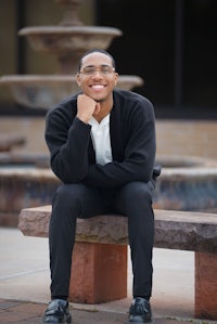 a young man sitting on a bench in front of a fountain